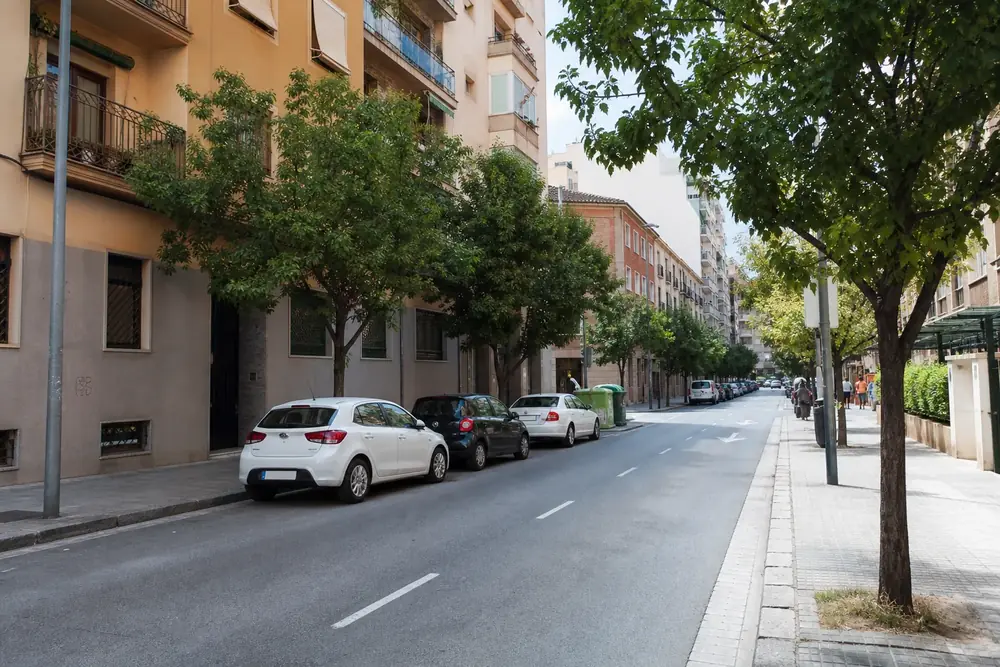Calle urbana de un carril por sentido con coches aparcados a ambos lados