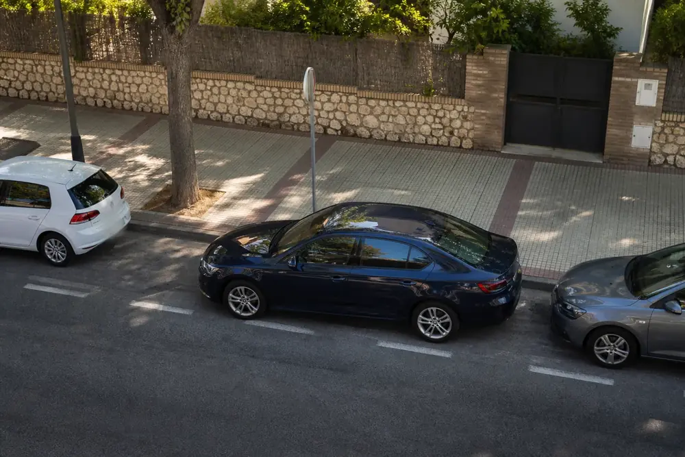 Coche estacionando en línea entre dos vehículos