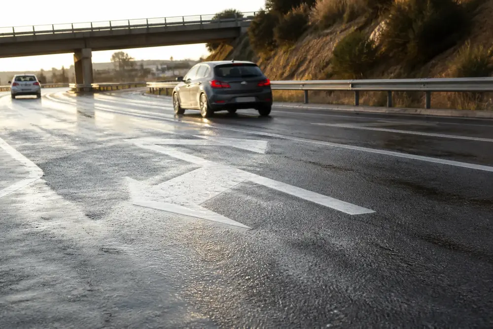 Flechas de selección de carril sobre calzada mojada bajo un viaducto
